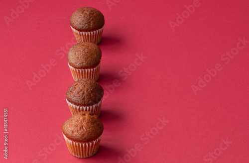 fresh mini cupcakes stand in a row on a red background. Muffins in paper forms. Confectionery background concept. Place for text. High quality photo