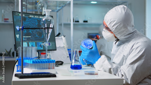 Chemist in ppe suit using micropipette for filling test tubes in modern equipped laboratory. Team of scientists examining virus evolution using high tech for vaccine development against covid19