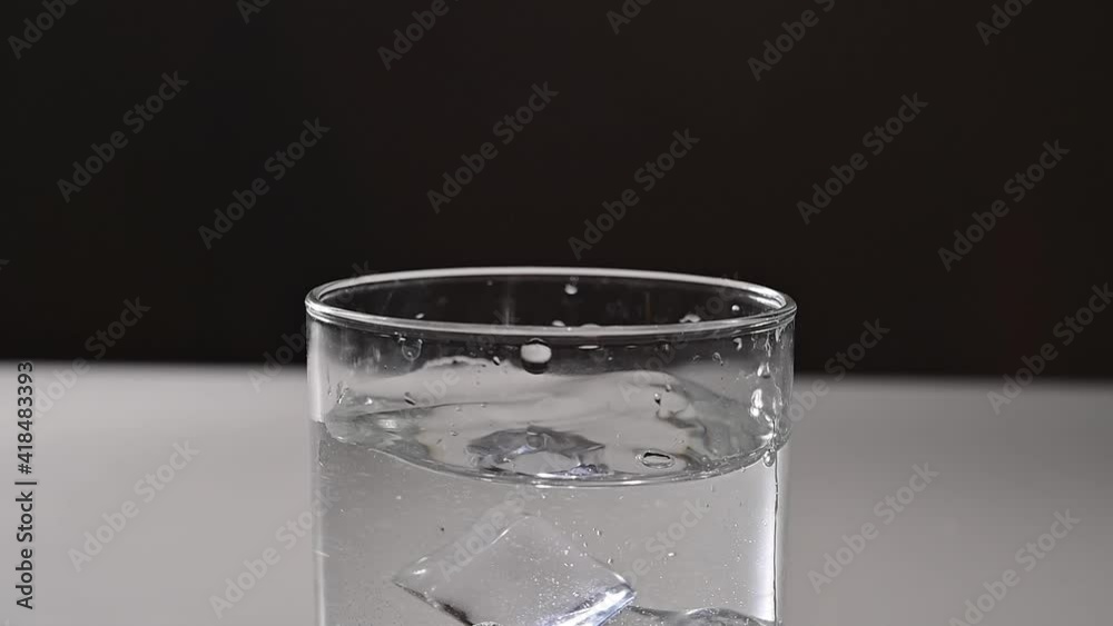 Ice falls into a glass of water. Ice falls into a glass of water.