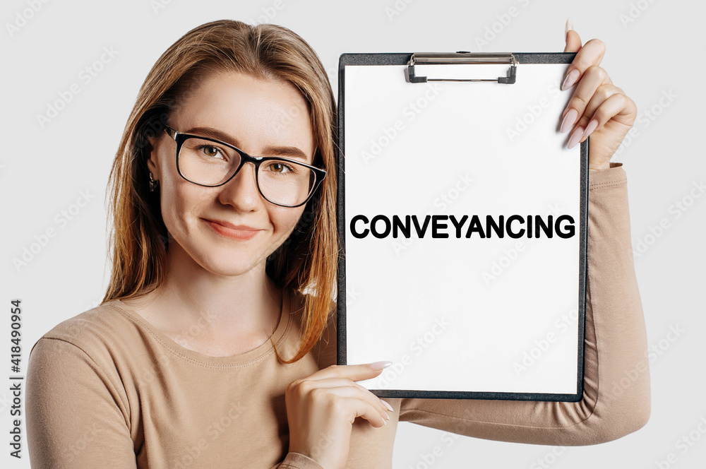 Conveyancing. Beautiful young business woman wearing glasses holds a clipboard with mock up space isolated on gray background Conveyancing. Beautiful young business woman wearing glasses holds a clipboard with mock up space isolated on gray background