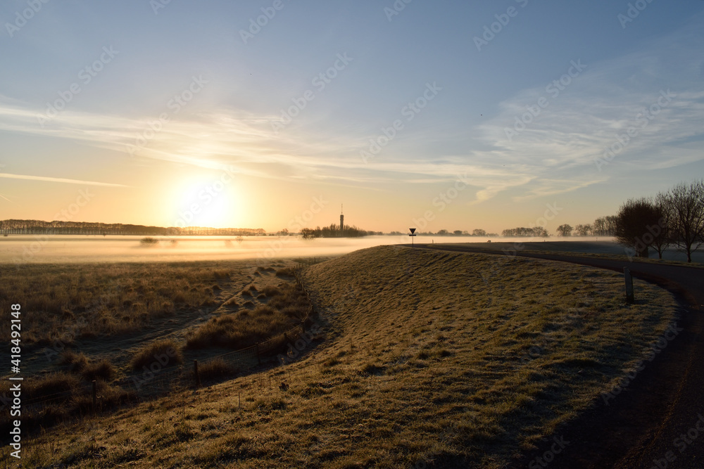A scenic view of a winding Dutch road overlooking a meadow filled with ground frost close to Oss, netherlands
