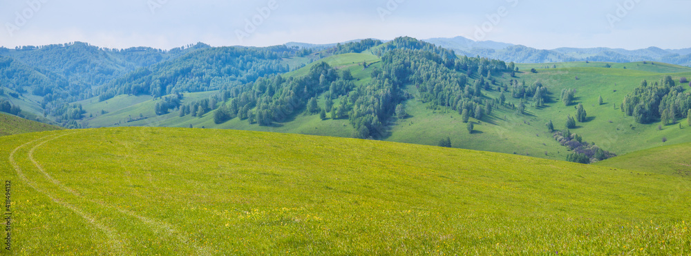 Picturesque valley, panoramic mountain view. Bright sunlight, spring greens of forests and meadows.