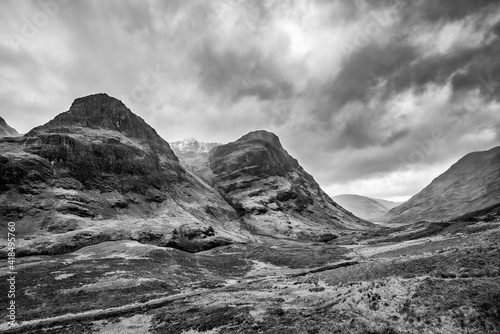 Majestic moody black and white landscape image of Three Sisters in Glencoe in Scottish Highlands on a wet Winter day wit high water running down mountains