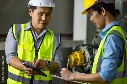 Senior and junior engineers talking together with intimated manner beside the machine in factory. Concept for good teamwork and unity of colleauges photo