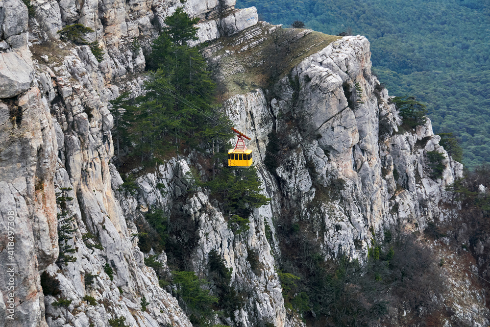 cabin of the aerial tram moves against the background of a steep rocky cliff cabin of the aerial tram moves against the background of a steep rocky cliff