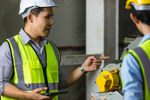 Senior and junior engineers talking together with intimated manner beside the machine in factory. Concept for good teamwork and unity of colleauges photo