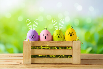 Easter holiday concept with colorful Easter eggs as cute bunny and chicken characters in box on wooden table over green bokeh background
