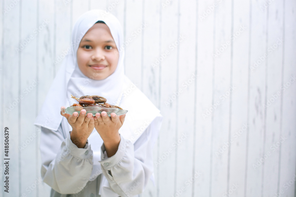 Young asian muslim woman wearing headscarf smiling to the camera while holding dates on the plate with copy space Young asian muslim woman wearing headscarf smiling to the camera while holding dates on the plate with copy space