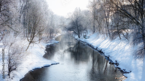 Amazing winter landscape in the public park. Scenic view of the river and reflection of frosty trees in the water. Panorama nature image. Selective focus.