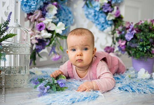 baby girl in a pink sundress lies with bouquets of flowers in a festive background