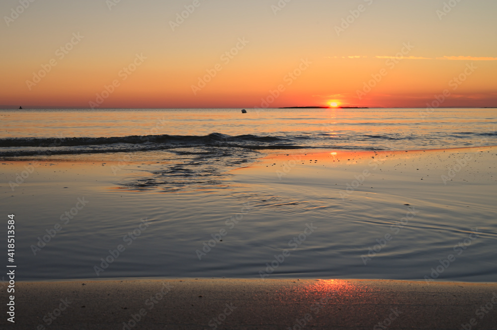 Tramonto sul mare con riflesso del sole sull'acqua e sulla sabbia.