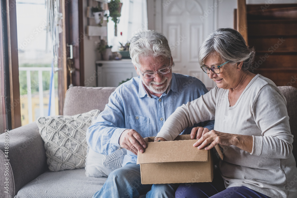 Happy mature aged older family couple unpacking carton box, satisfied with internet store purchase or unexpected gift, feeling excited of fast delivery shipping service, positive shopping experience.. Happy mature aged older family couple unpacking carton box, satisfied with internet store purchase or unexpected gift, feeling excited of fast delivery shipping service, positive shopping experience..