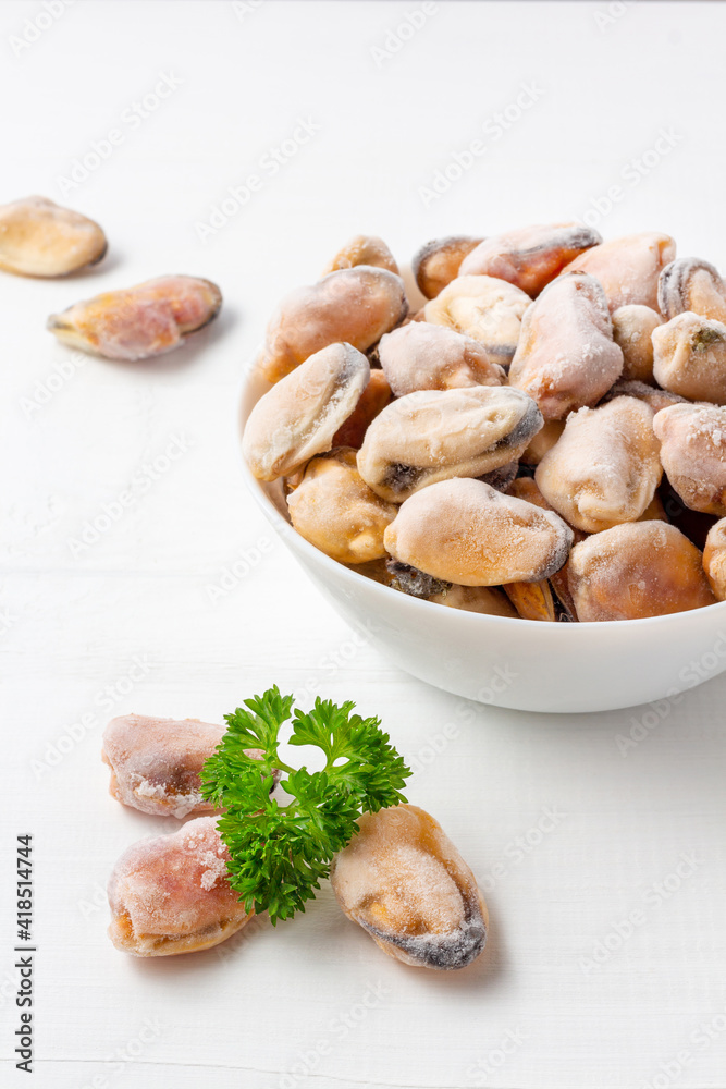 A bowl of frozen mussels with parsley on white wood background. Healthy seafood for mediterranean diet. A bowl of frozen mussels with parsley on white wood background. Healthy seafood for mediterranean diet.