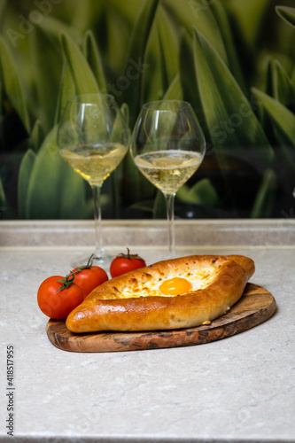 Khachapuri with egg on a wooden tray with wine and tomatoes