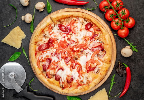pizza with sausages, mushrooms, tomatoes and cheese on a stone background
