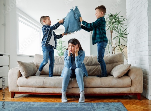 mother son family tired headache problem jumping hyperactive child boy kid sofa pillow photo