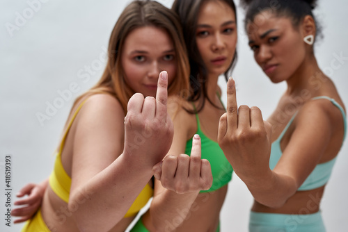 Single and proud. Studio shot of confident young women in colorful underwear showing fourth finger without ring, posing together isolated over light background