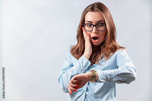 beautiful girl in a blue shirt and glasses looks at the clock on a white background. isolated