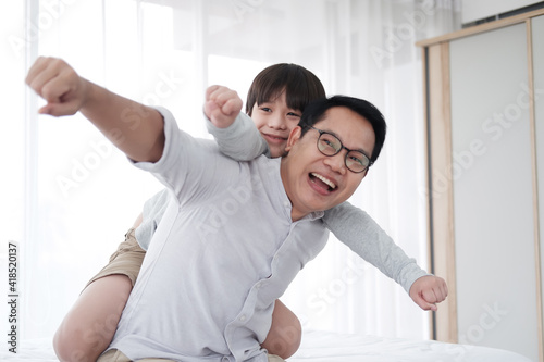 Smiling Asian cute little boy is relaxing and playful with father in bedroom at home. Family love and child educational for homeschool on holiday concept. Focuc at asian boy.
