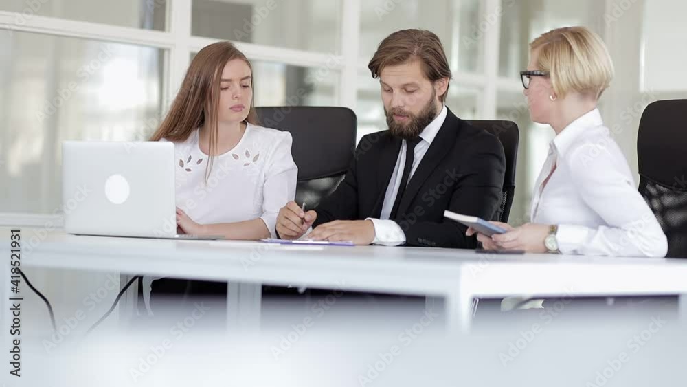 Three colleagues working together discussing the project teamwork. The man explains the work to his colleagues in the corporate team, collaborating, talking in the office Three colleagues working together discussing the project teamwork. The man explains the work to his colleagues in the corporate team, collaborating, talking in the office