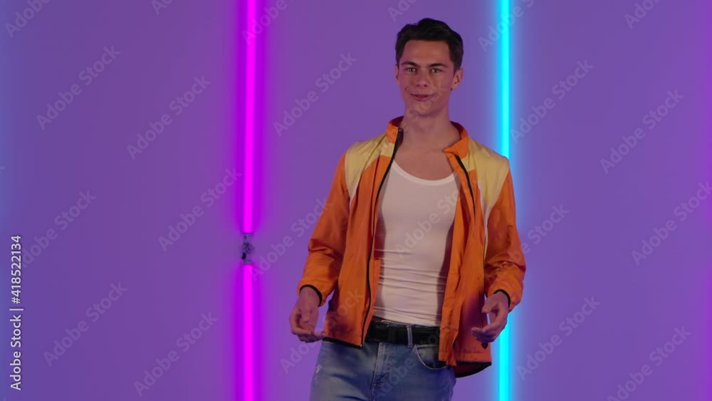 Portrait of stylish guy looking at the camera with wow delight and joy. Male fashion model in yellow jacket poses in dark studio against the backdrop of bright neon lights. Slow motion. Portrait of stylish guy looking at the camera with wow delight and joy. Male fashion model in yellow jacket poses in dark studio against the backdrop of bright neon lights. Slow motion.