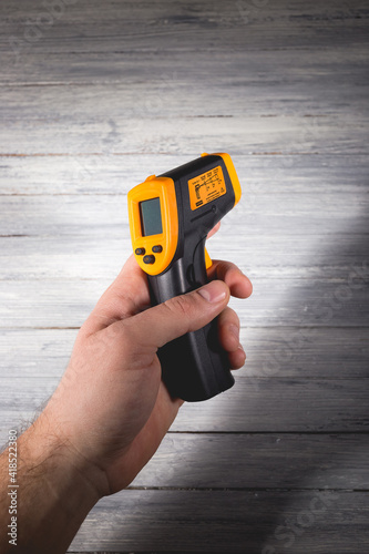 A man holds a yellow-black pyrometer on a wooden background. A device for non-contact temperature measurement. photo