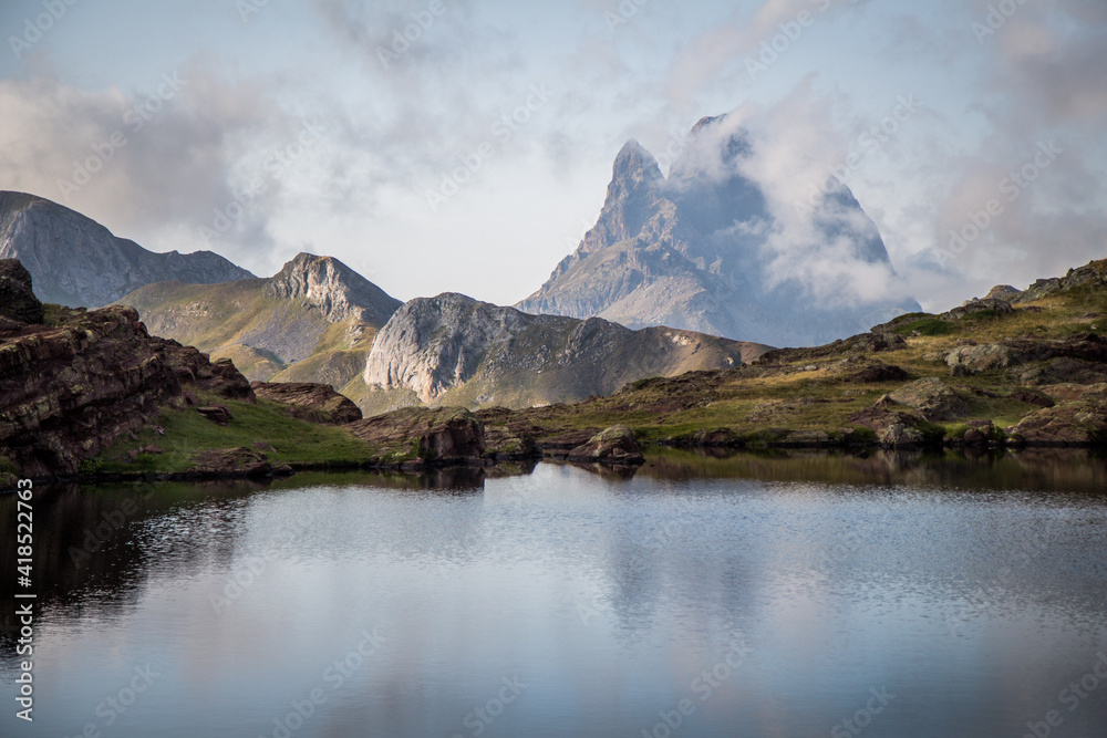 Stunning view of a beautiful mountain surrounded by clouds in the Pyrenees with a quiet lake in the foreground