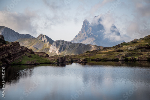 Stunning view of a beautiful mountain surrounded by clouds in the Pyrenees with a quiet lake in the foreground © Adrian Azorin
