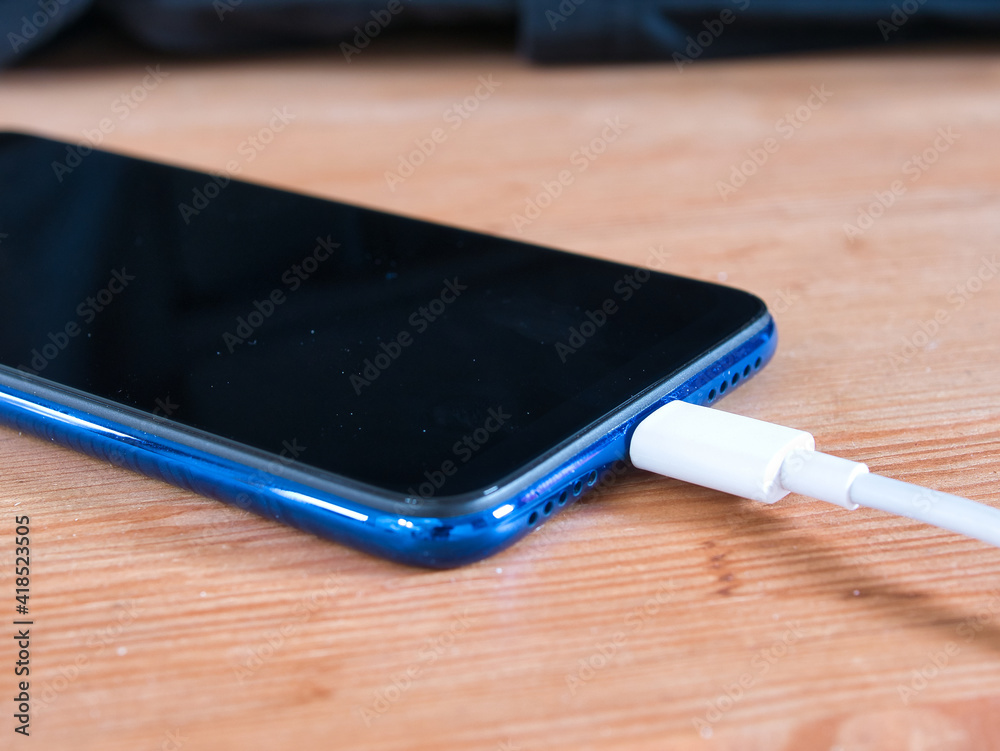 a mobile phone is lying on a wooden table while the battery is being charged a mobile phone is lying on a wooden table while the battery is being charged