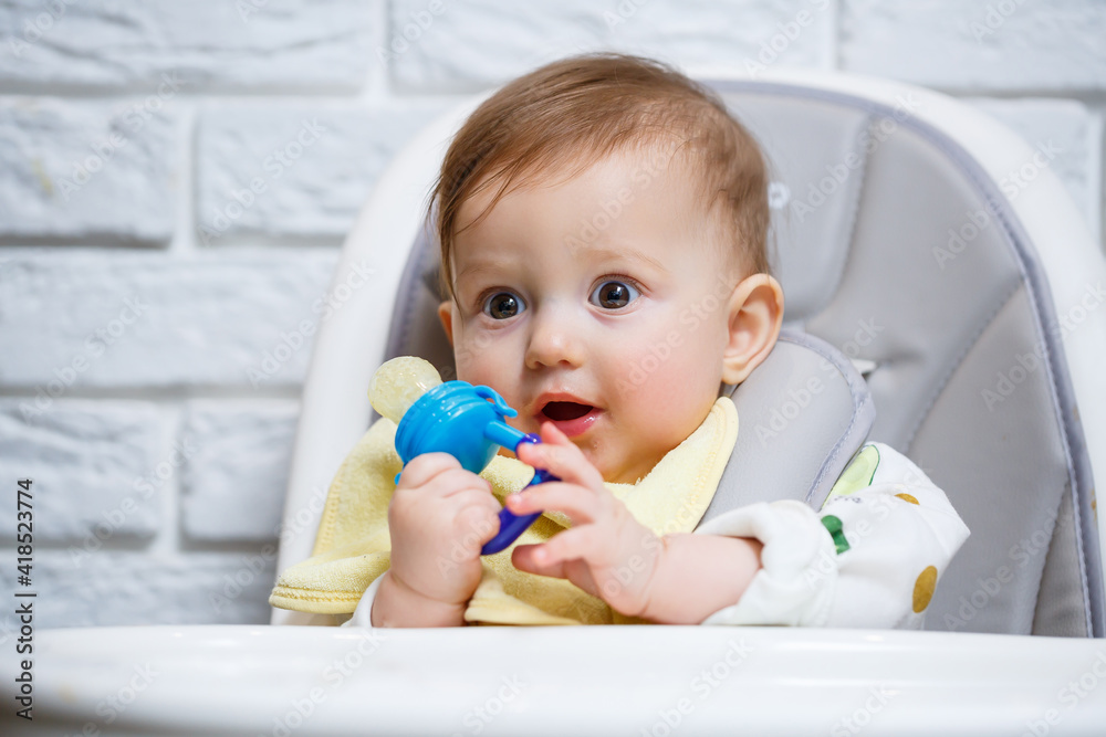 A small child sits on a high chair and eats fruits through the net. Nibbler for feeding babies A small child sits on a high chair and eats fruits through the net. Nibbler for feeding babies