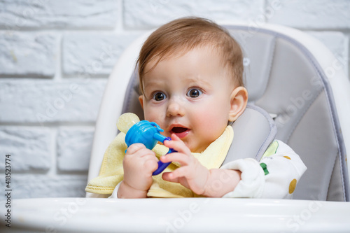 A small child sits on a high chair and eats fruits through the net. Nibbler for feeding babies photo
