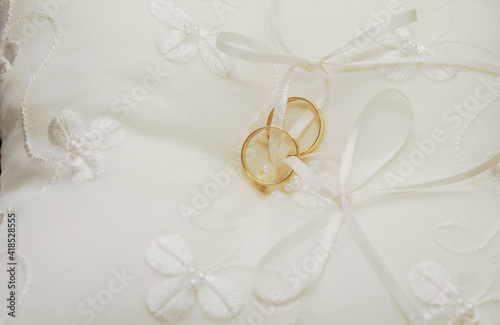 Dos anillos de oro unidos a un pequeño cojín blanco con flores bordadas. Vista cercana de las joyas para el día de la boda.
