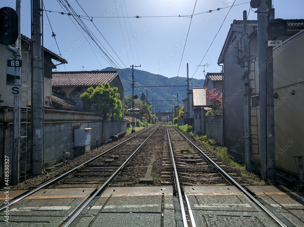 KYOTO, JAPAN - APRIL 5, 2018: Railroad tracks in the city of Arashiyama, Kyoto. The railway goes into the distance to the station, along the tracks there are houses with cherry blossoms.
