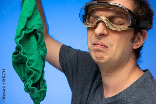 Caucasian male wearing goggles making disgusted face gesture at smelly green underwear held in hand studio shot photo