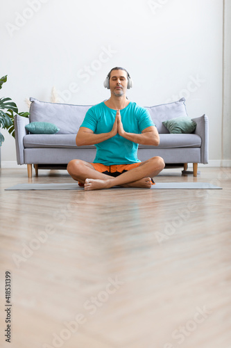 Workout at home. Middle aged man meditating while doing yoga. Vertical photo.