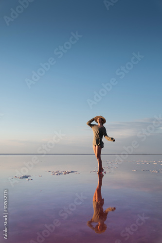 Evening view of the shallow salty pink lake. Reflection. A young woman in a hat walks on the water and is reflected. Silence and harmony. Happiness.