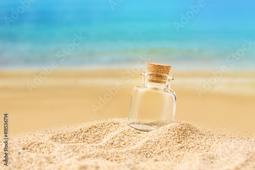 bottle on sand beach over blurred tropical blue sea and clear blue sky.