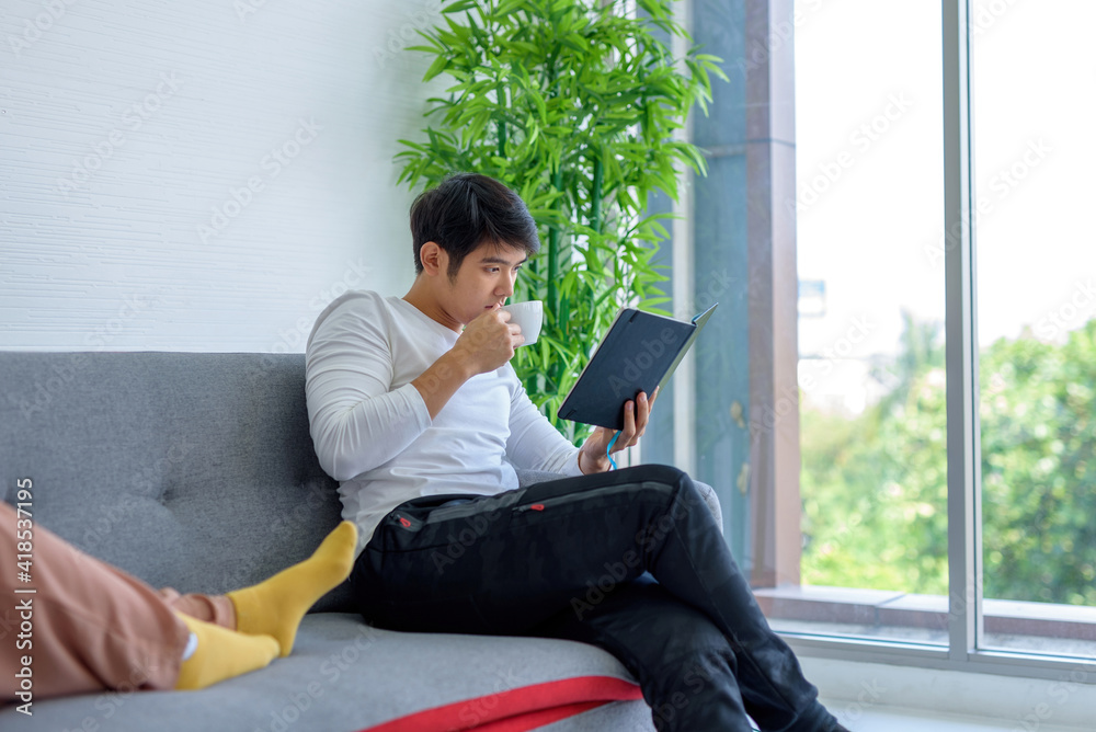 A teenager sipping coffee and reading a relaxing book in his living room.. A teenager sipping coffee and reading a relaxing book in his living room..