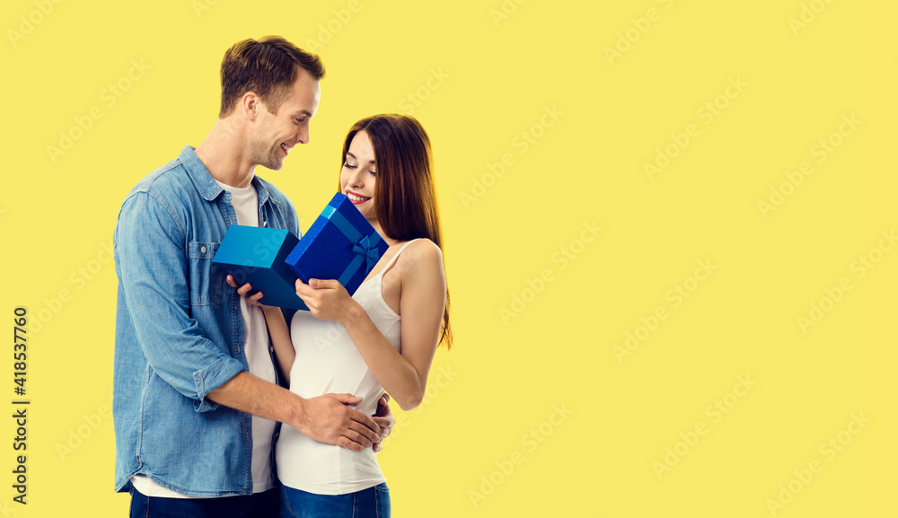 Naklejka premium Love, dating, celebrating, lovers concept - happy smiling amorous couple opening gift box. Studio portrait of young man and woman, isolated over yellow background.