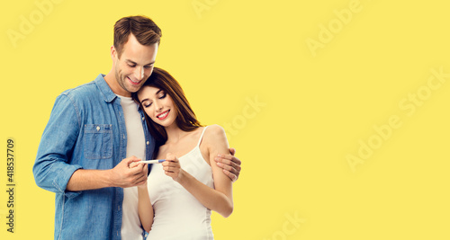 Love, relationship, new parents and happy family concept - couple, finding out results of a pregnancy test. Studio portrait of young man and woman, isolated over yellow background.