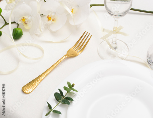 Beautiful romantic table setting with gold cutlery, orchid and white empty plate on white background