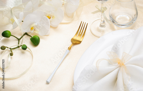 Festive spring table setting with white napkin and white orchids on beige silk tablecloth