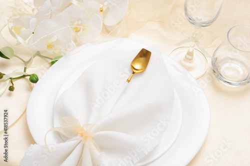 Beautiful festive table setting with white napkin and white orchids and golden cutlery on light background