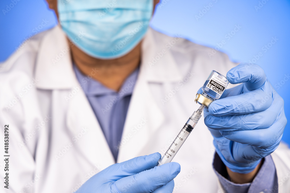 Close-up and focus on syringe inserted into Covid-19 vaccine vial by Asian medical doctor with medical glove in background Close-up and focus on syringe inserted into Covid-19 vaccine vial by Asian medical doctor with medical glove in background