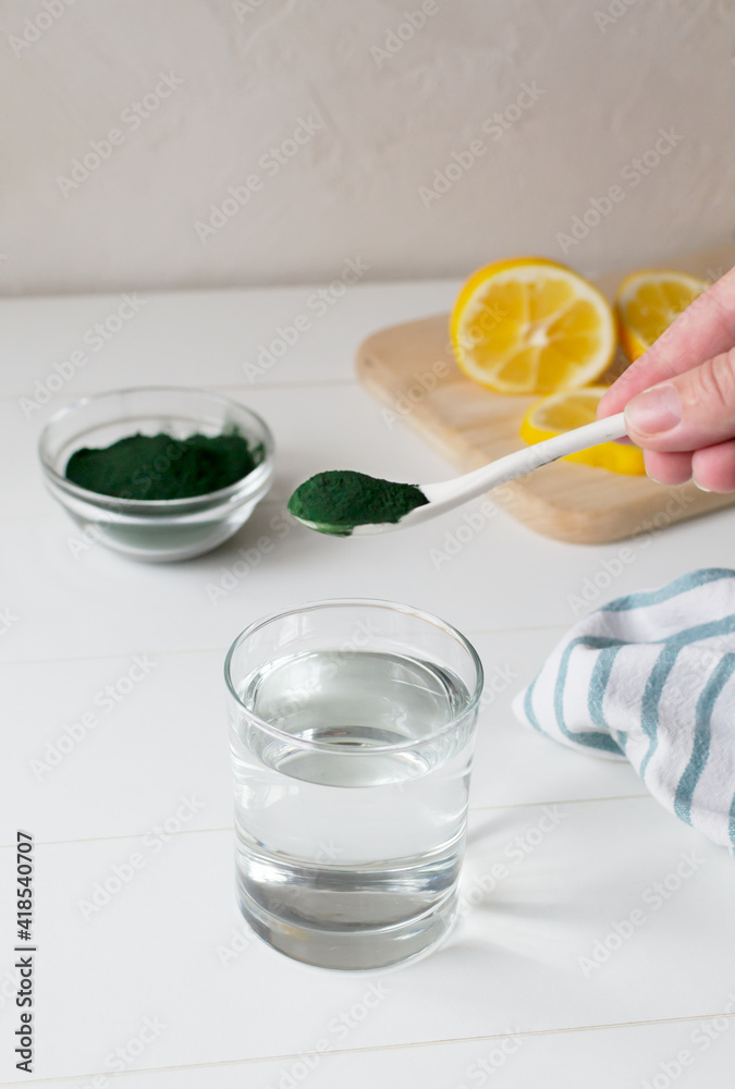 A glass of water and a teaspoon of spirulina in your home kitchen. Healthy food concept. Vertical orientation. Copy space. A glass of water and a teaspoon of spirulina in your home kitchen. Healthy food concept. Vertical orientation. Copy space.