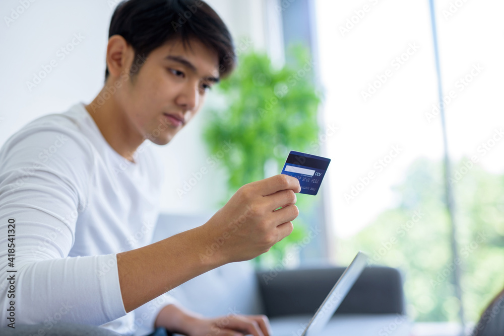 An Asian man holding a blue pop up credit card and looking at it in order to use it.. An Asian man holding a blue pop up credit card and looking at it in order to use it..