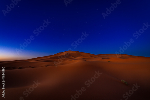 View of the beautiful Erg Chebbi dunes at night, under a deep blue sky with stars.