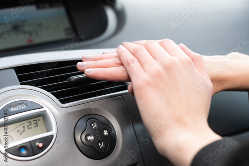 The woman warms her hands over the car's hot air outlet. Cold hands.