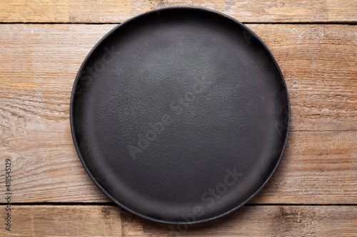 Empty cast iron frying pan on wooden culinary background. Space for text.