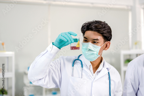A scientist holding a beaker and looking at chemicals In it Inside the laboratory